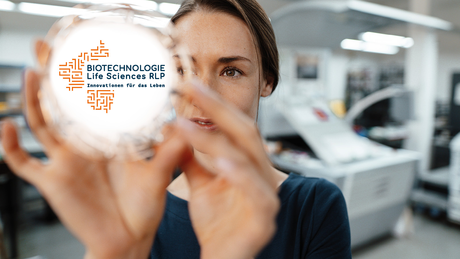 [Translate to English:] Frau hält eine Glaskugel, die das Logo "Biotechnologie Life Sciences RLP - Innovation fürs Leben" trägt